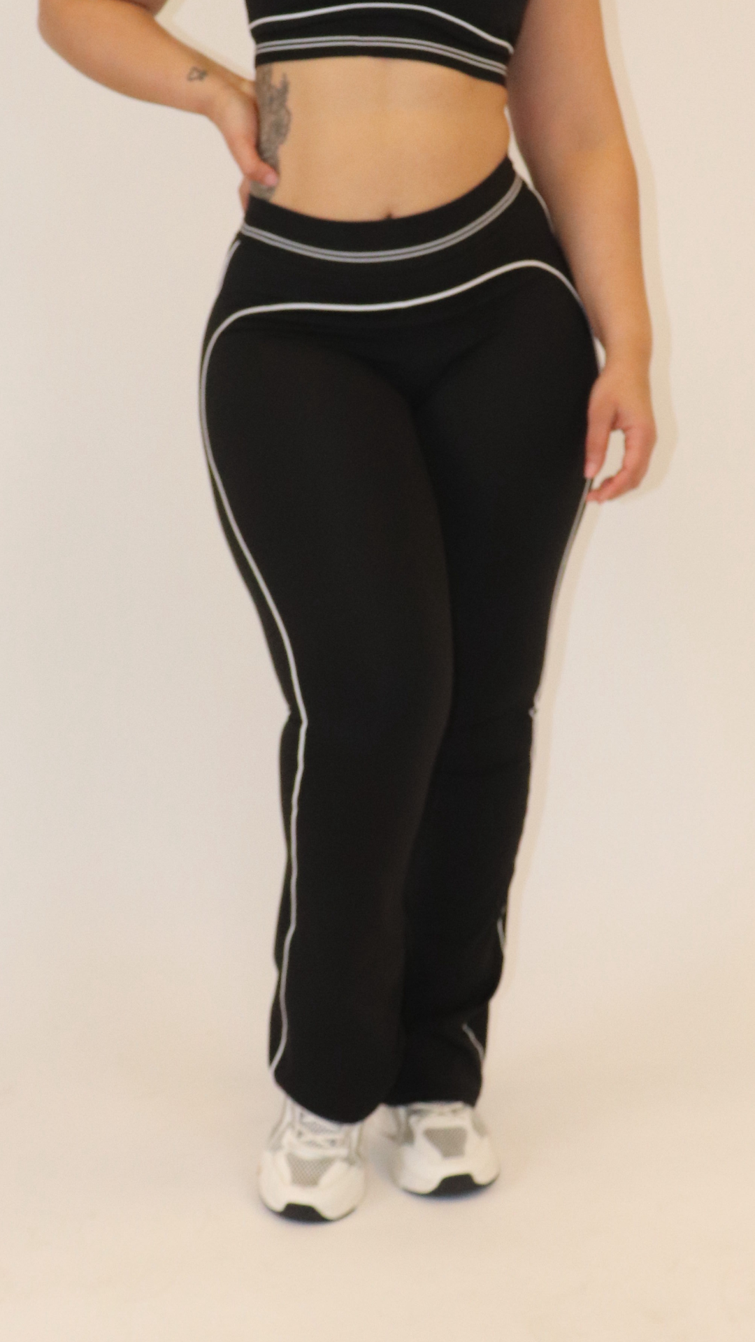 Person wearing black pants with white stripes on a plain background